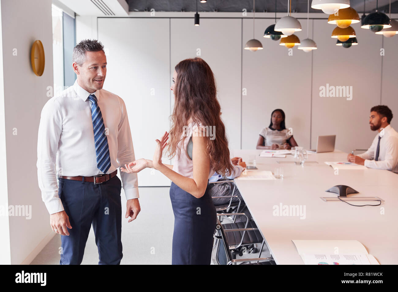 Businessman And Businesswoman Standing In salle moderne d'avoir une discussion informelle avec des collègues autour de la table de réunion en arrière-plan Banque D'Images