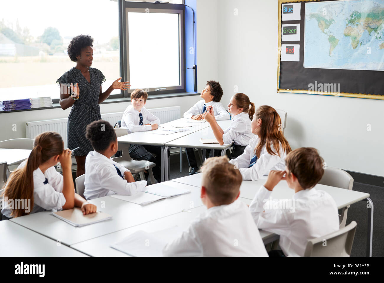 Tuteur Secondaire Comité permanent par des tables avec des étudiants en uniforme Leçon d'enseignement Banque D'Images