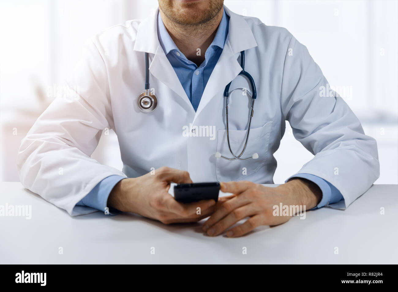 Consultation médicale en ligne - médecin assis par le tableau de l'office et à l'aide de smart phone Banque D'Images