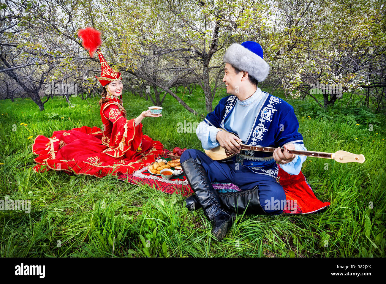 Femme Kazakh avec plateau et homme jouant de la dombra instrument sur l'herbe verte dans le jardin d'apple d'Almaty, Kazakhstan, en Asie centrale Banque D'Images