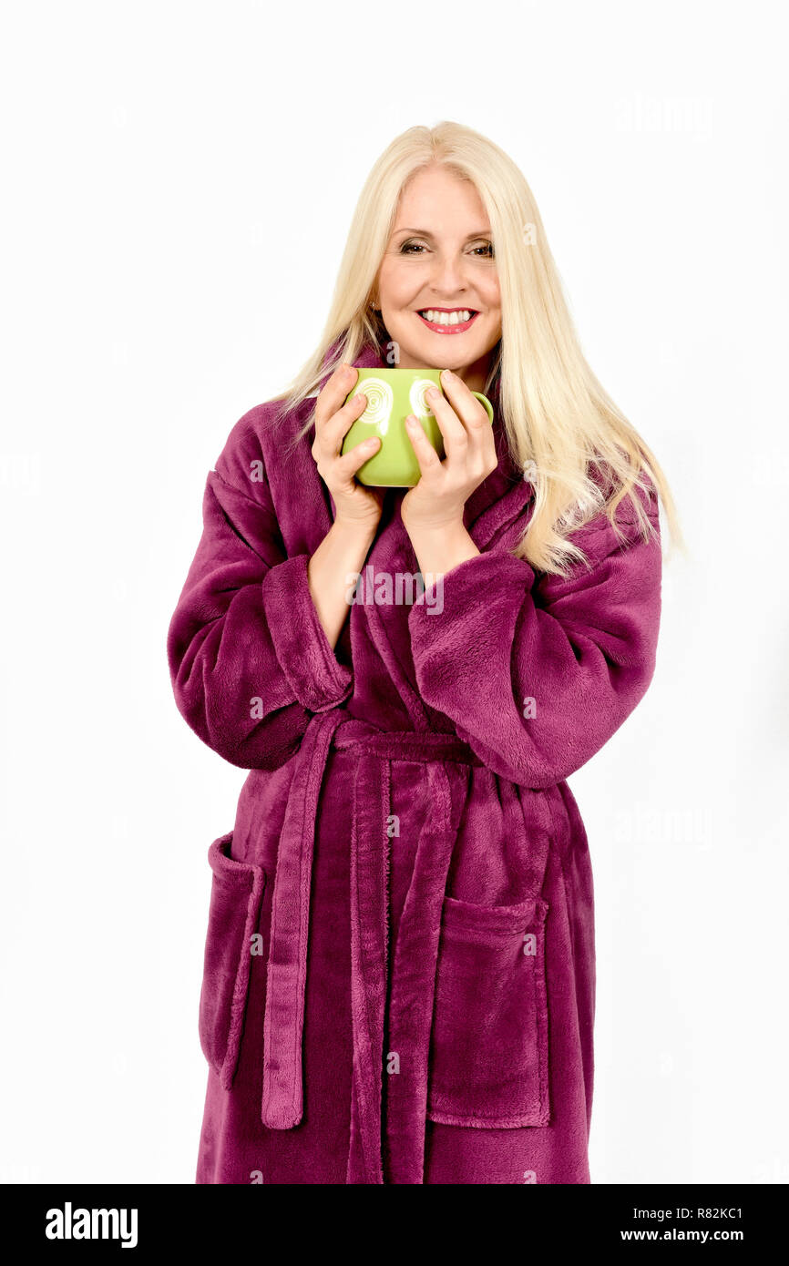 Jolie femme en robe de chambre pourpre fluffy se tenant la main autour d'une tasse de thé, prises contre fond blanc Banque D'Images