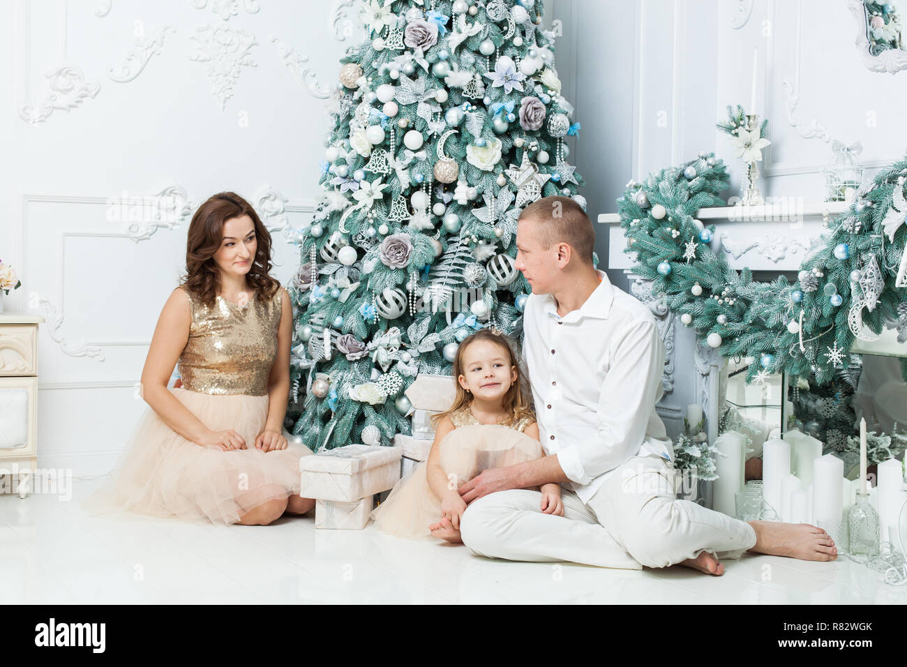 Jeune famille avec fille assis près de l'arbre de Noël par la cheminée. Banque D'Images