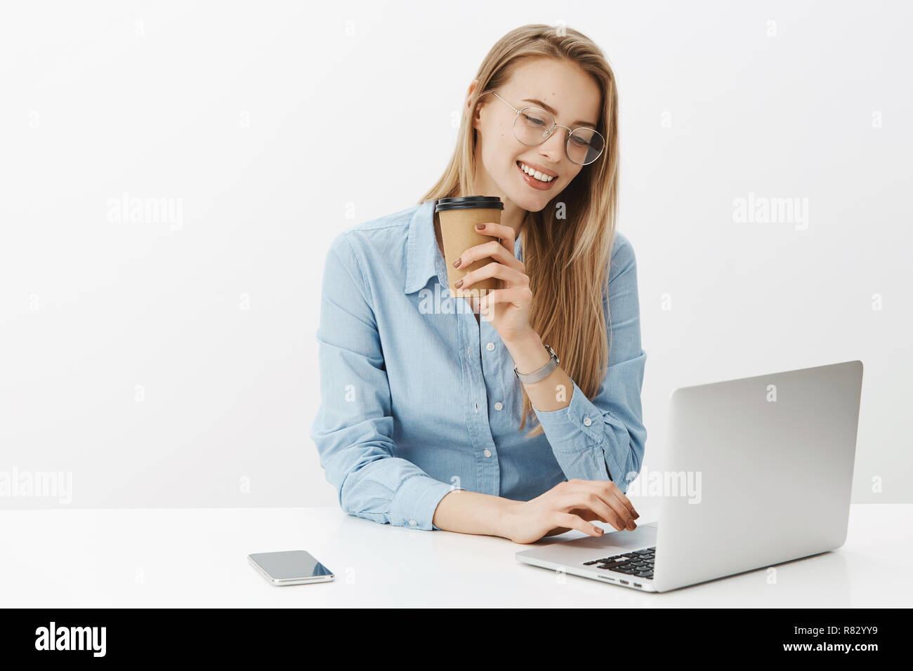 Freelenace, digital nomad et van life concept. Détendue et insouciante attractive blonde woman in glasses working on laptop smiling joyeusement comme boire du café pendant le travail sur fond gris Banque D'Images