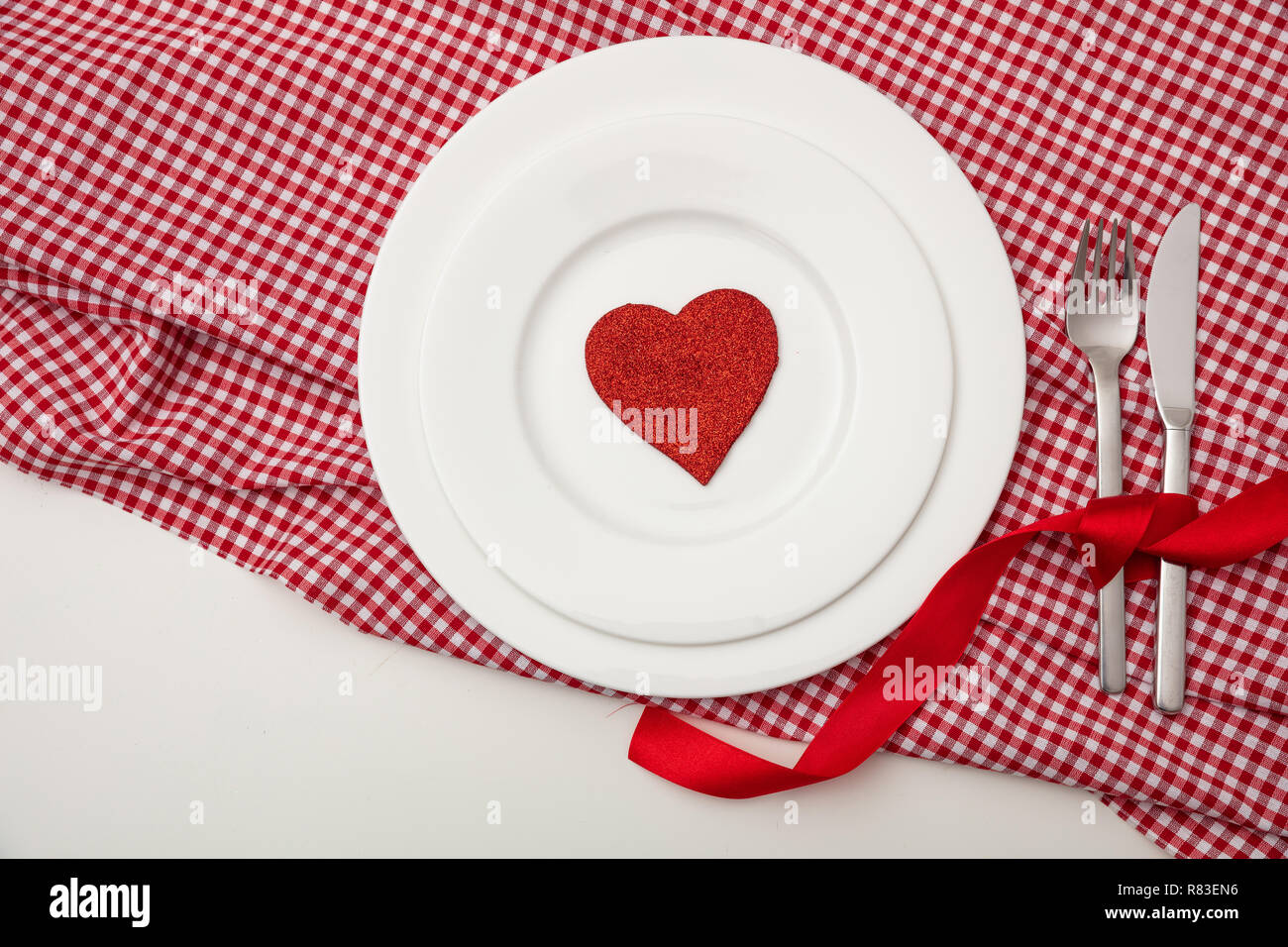 Valentines Day dîner, table, place. Cœur rouge sur les plaques blanches, rouge à carreaux tapis de table, fond blanc, copie de l'espace, vue d'en haut. Banque D'Images