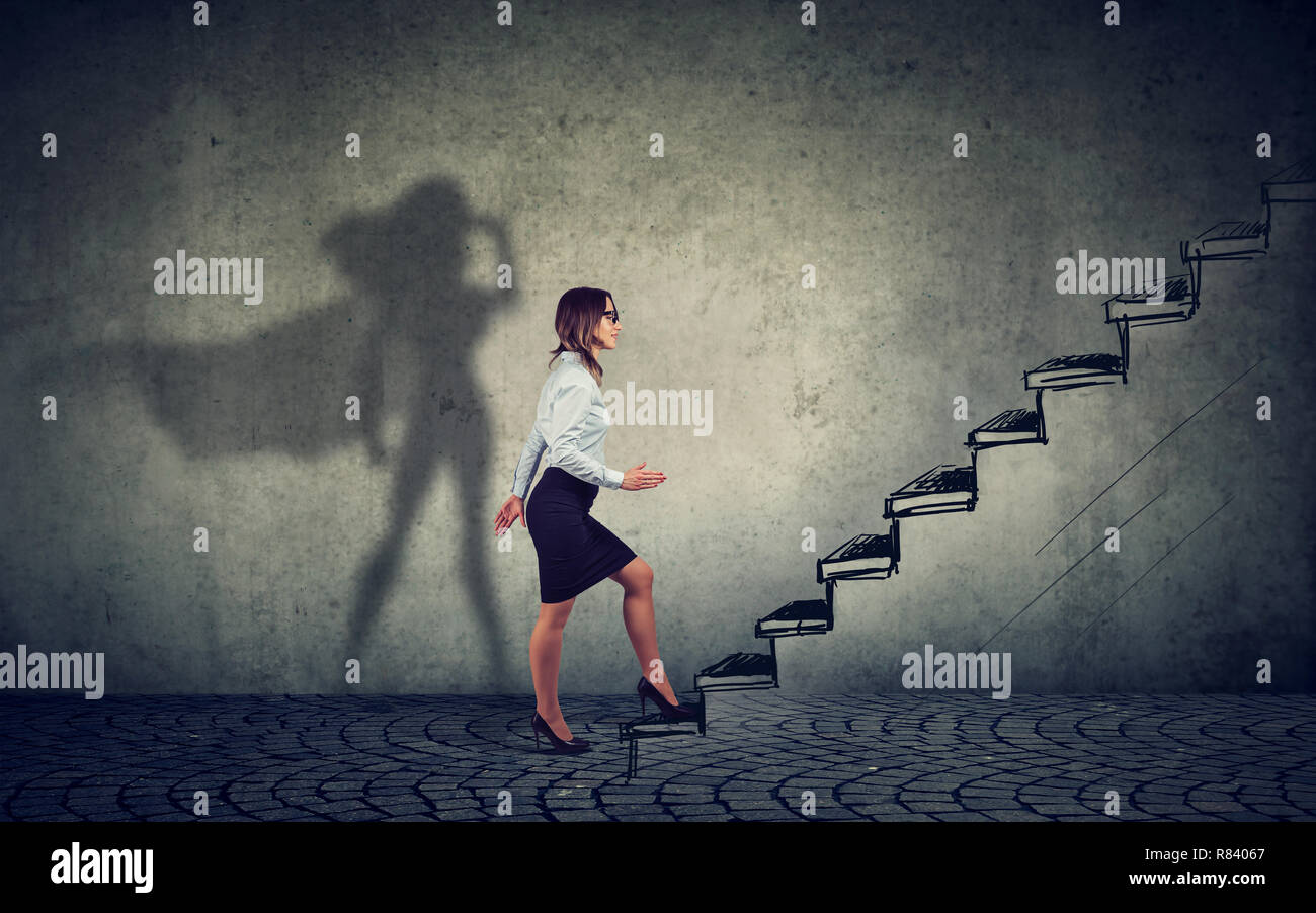 Super Hero business woman intensifier dans les escaliers en montant vers le succès sur fond de mur gris Banque D'Images