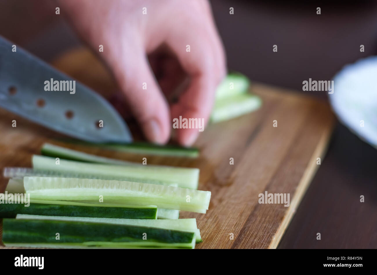 Woman's Hands Cut Allumettes de concombre avec Couteau Santoku sur une planche à découper en bois. Salades, Maki et Temaki Sushi Rolls Ingredient Banque D'Images