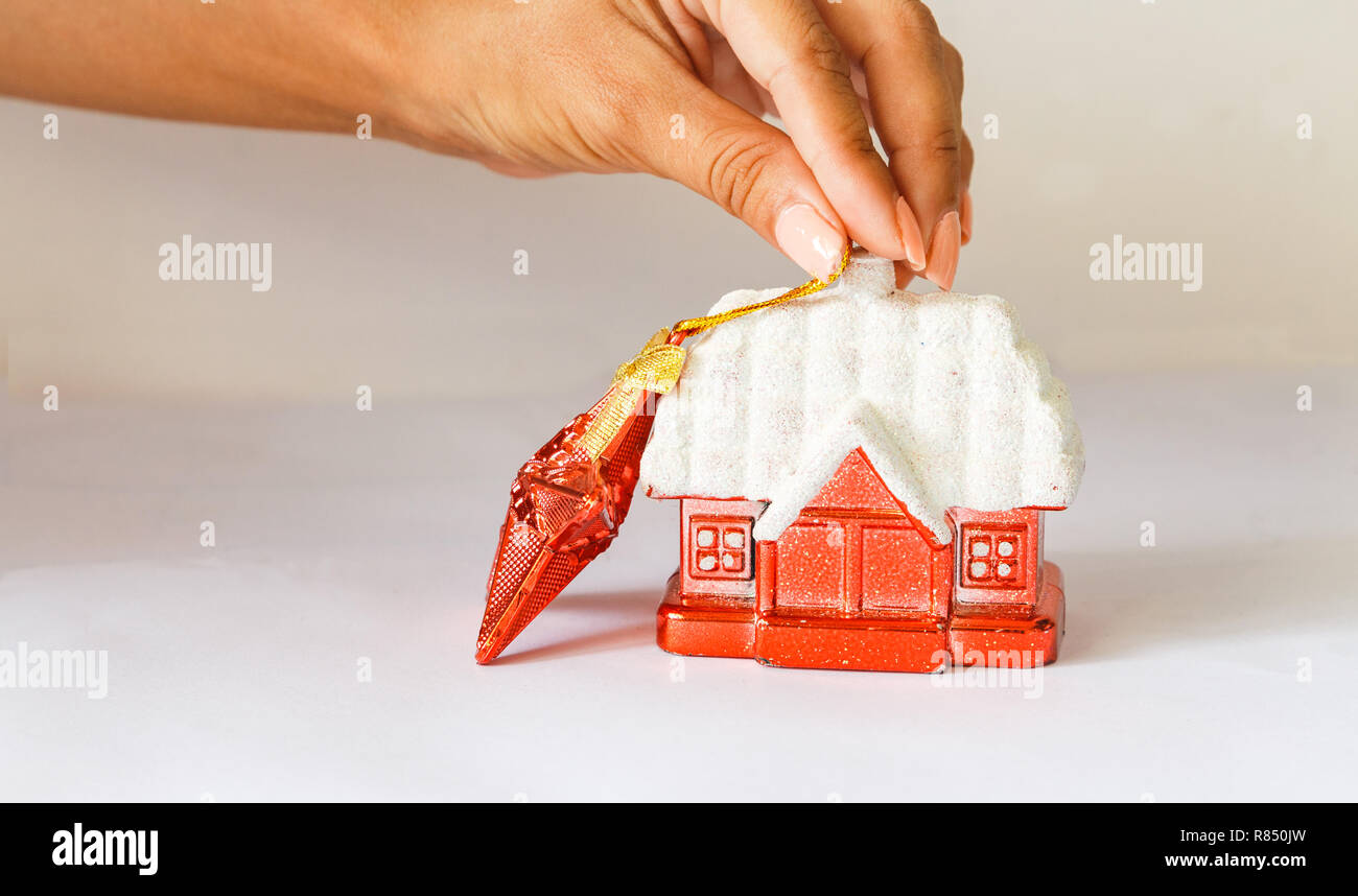 Décoration Nouvel An. red hut avec un toit couvert de neige et une étoile rouge sur un fond blanc. femme main tenant une étoile. Banque D'Images