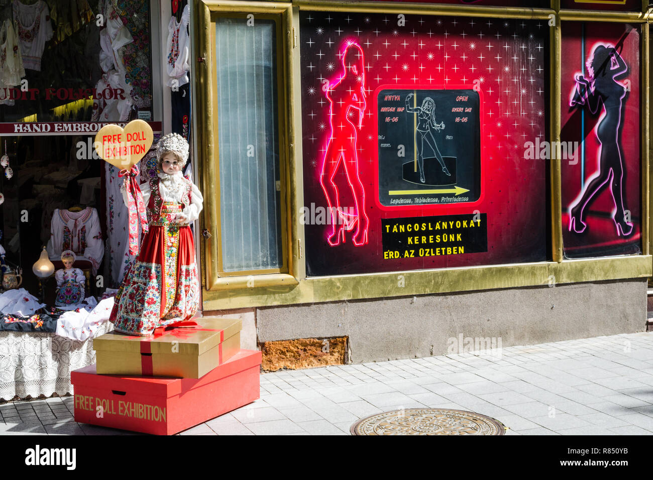 Poupée fille dans des vêtements traditionnels européens devant un magasin de poupées et à côté d'un club de strip, Budapest, Hongrie Banque D'Images
