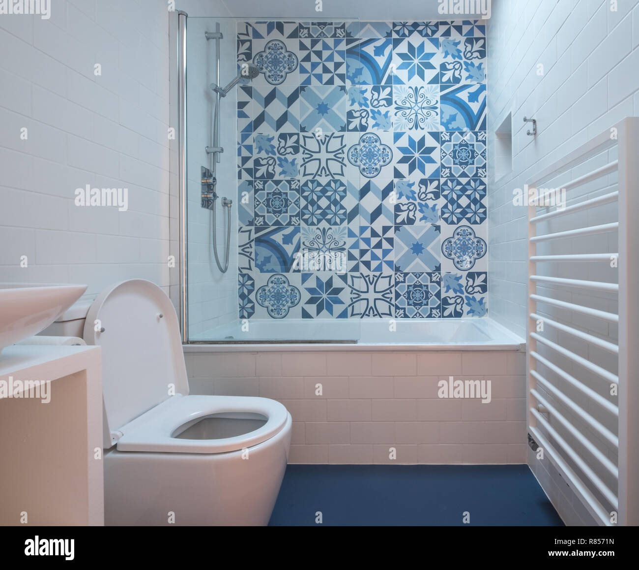 Salle de bains moderne avec baignoire, toilettes, niche dans le mur et  l'unité de bassin, sol en caoutchouc bleu et bleu et blanc carreaux de  mosaïque au-dessus de la baignoire Photo Stock -