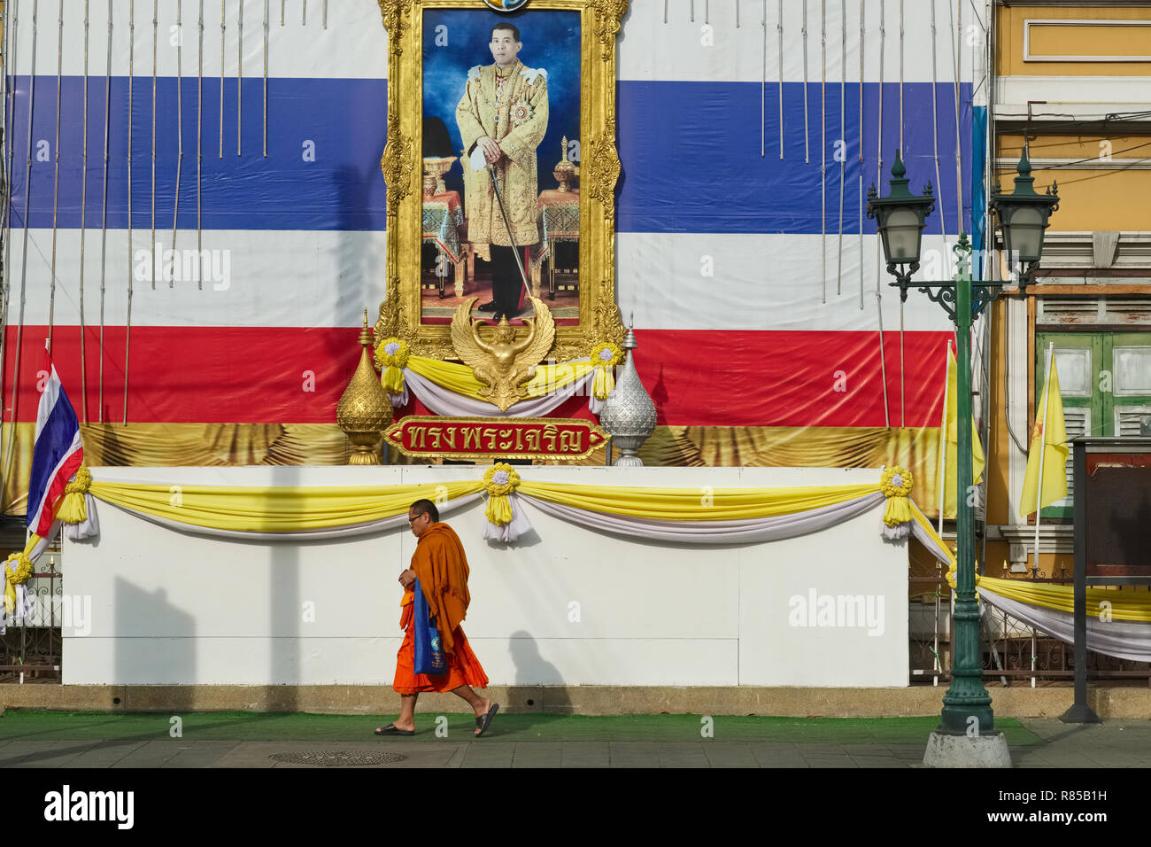 Un moine bouddhiste thaï géant passe sous un drapeau et un portrait du roi Maha Vajiralongkorn, en face de l'école Gulab Suan, Bangkok, Thaïlande Banque D'Images