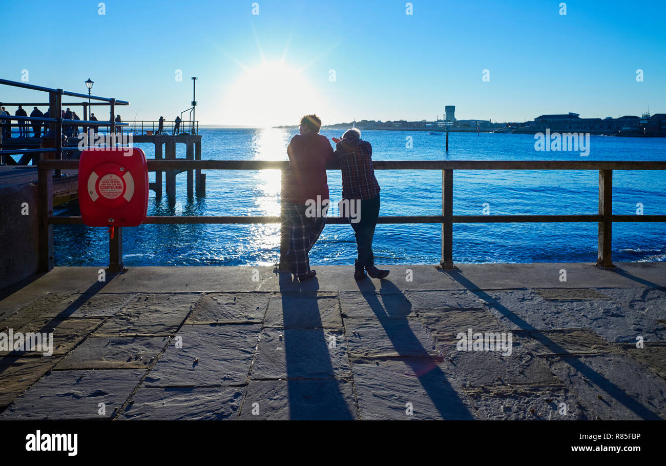 Couple en premier plan avec vue sur l'entrée du port de Portsmouth avec de très longues ombres et dans le soleil Banque D'Images
