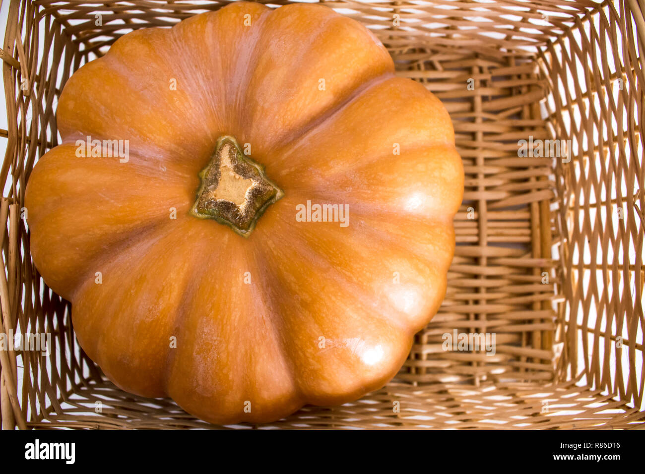 Mise à plat de belle orange citrouille se reposant dans un panier en osier rustique. Banque D'Images