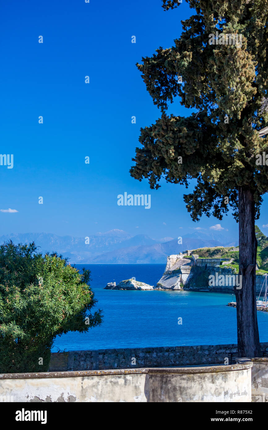 Vue paysage ensoleillé, jour de printemps à Corfou, l'île de Kerkira, Grèce. Paysage bleu vertical, avec bush partielle et arbre à l'avant le long de la promenade. Banque D'Images