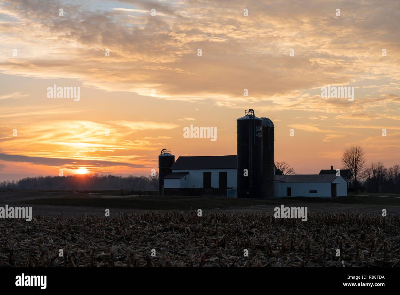 Coucher de soleil sur la ferme du Midwest avec grande grange, silos et champ de maïs récolté. Banque D'Images