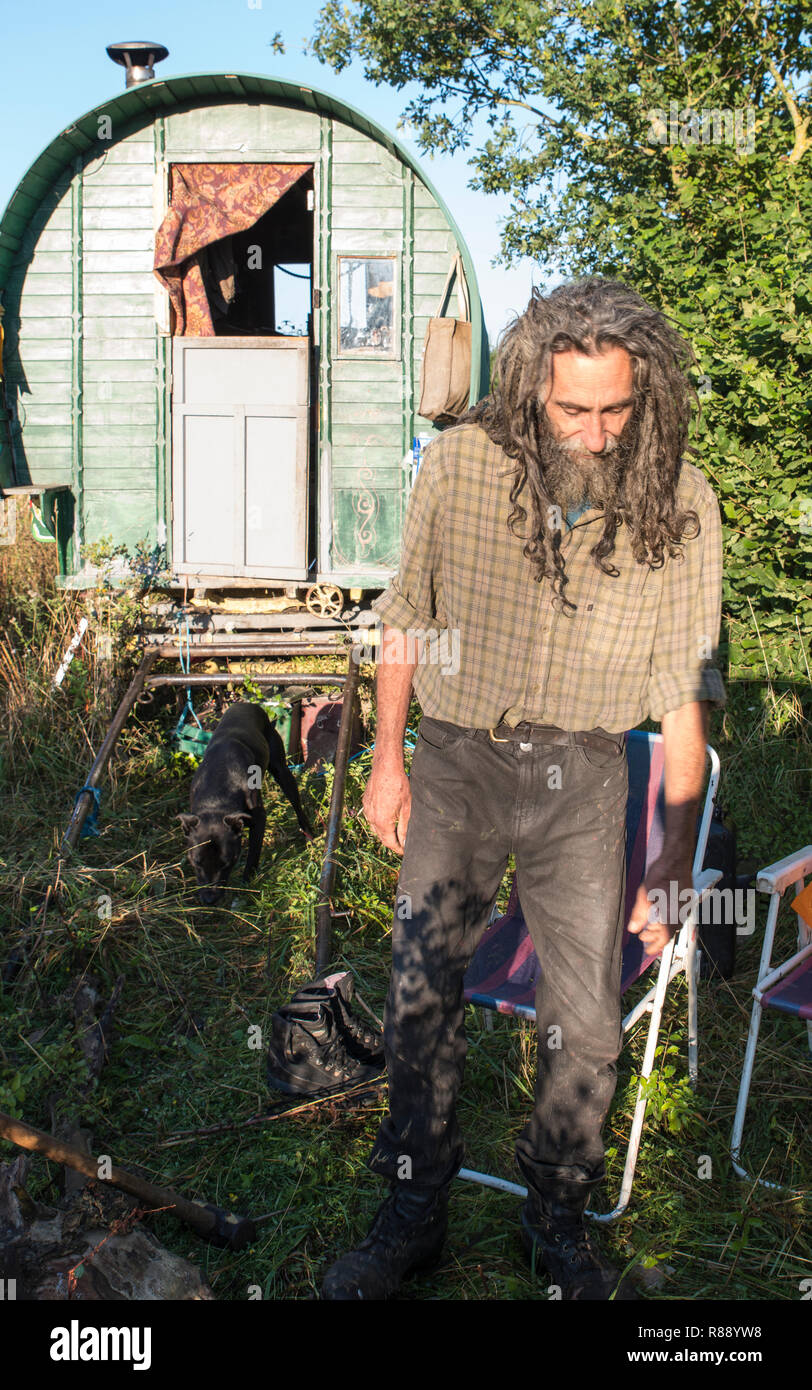 Peter le voyageur avec de longs cheveux et la barbe en désordre devant sa roulotte itinérante en bois sur un bord de la route. Banque D'Images