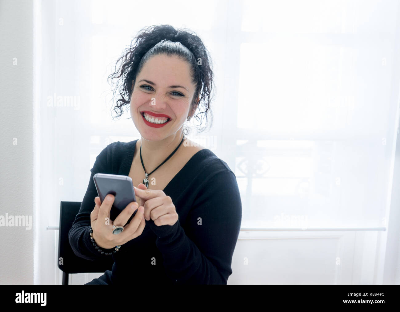 Portrait d'une belle femme normale en utilisant son téléphone portable et souriant aux cheveux noirs, la peau blanche et rouge lèvres. Copy space Banque D'Images
