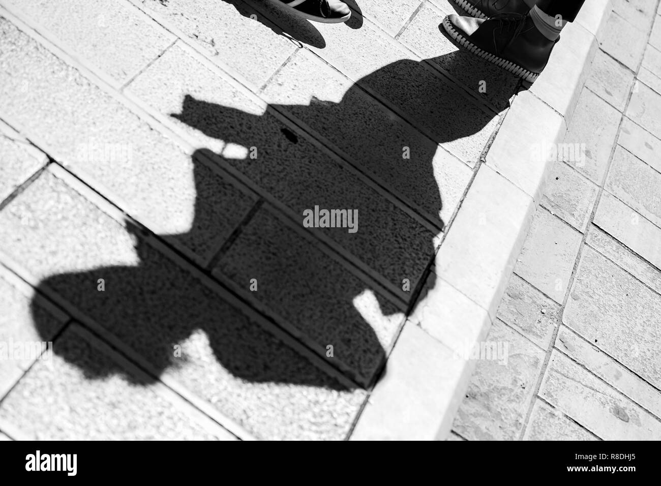 En diagonale composé photo de l'ombre d'un homme avec des chaussures de sport debout sur un patio en pierre dans la ville de Corfou en Grèce, noir et blanc Banque D'Images