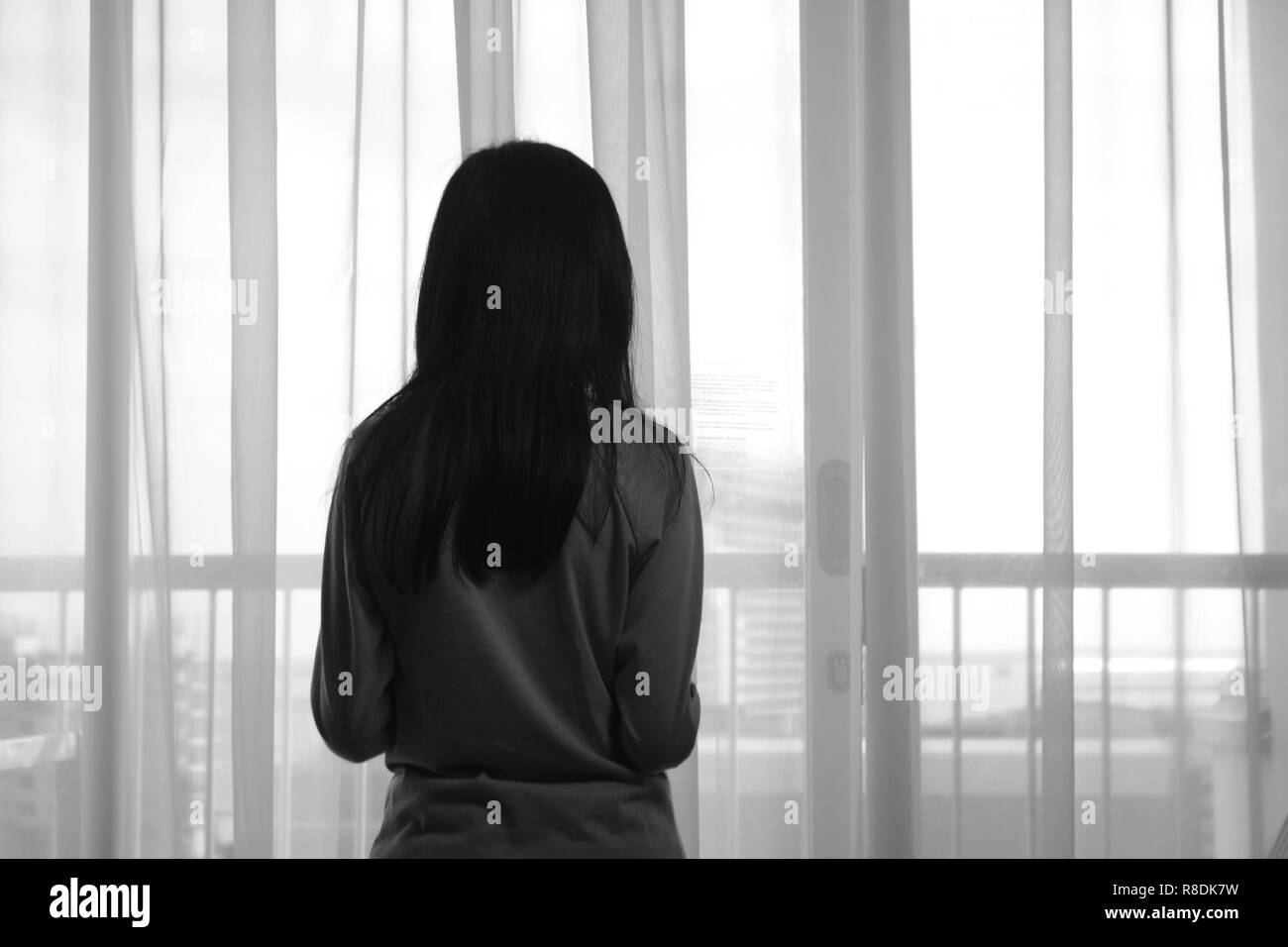 Vue arrière de l'image triste fille solitaire à travers la fenêtre en noir et blanc photo monochrome Banque D'Images