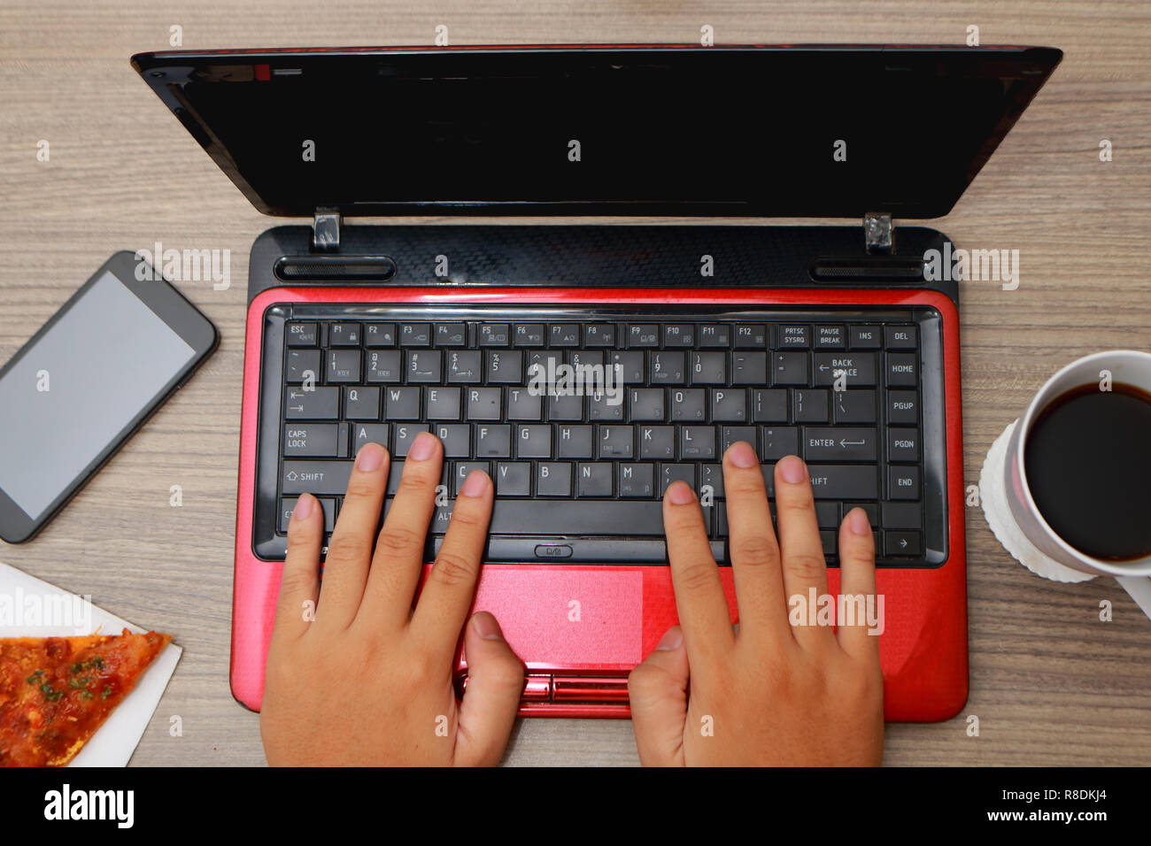 Vue du dessus de la main des hommes de la saisie sur ordinateur portable sur un bureau de travail avec pizza, café et téléphone cellulaire Banque D'Images