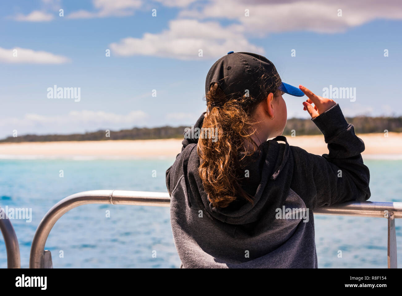 Enfant tenant sa casquette alors qu'elle regarde d'un bateau sur une plage proche près de Moreton Island, Queensland, Australie Banque D'Images