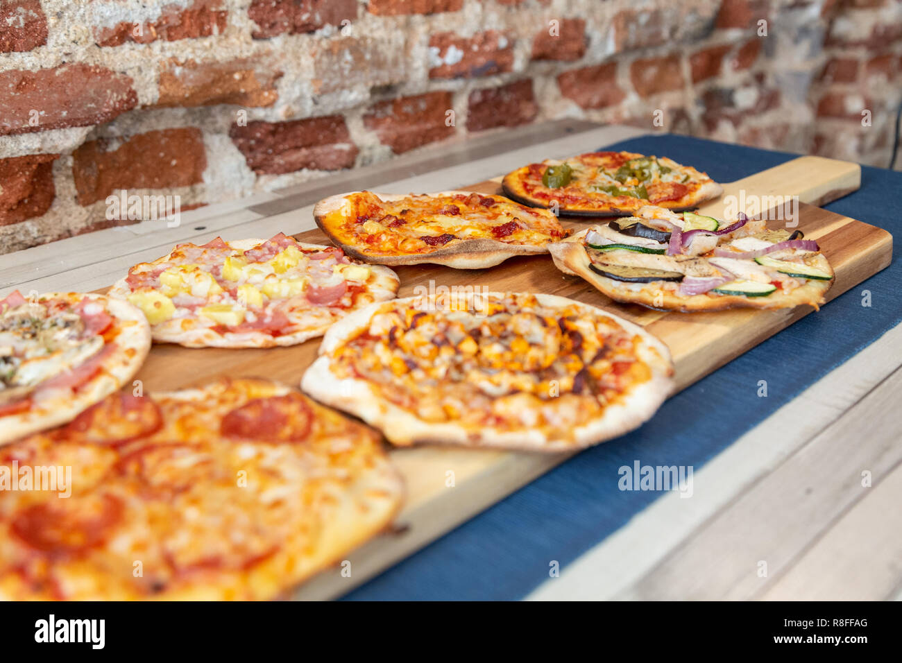 Sept petites pizzas sur une planche en bois, fraîchement sorti du four,  prêt à manger sur un restaurant. avec l'accent dans les légumes de la pizza.  Sur une table en bois avec