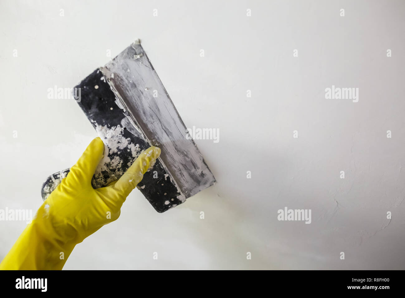 Dans la main du travailleur gants jaune tenant une spatule qu'un trou à l'aide d'une spatule avec du plâtre ou du mastic dans mur blanc. Processus de rénovation et de réparation, re Banque D'Images
