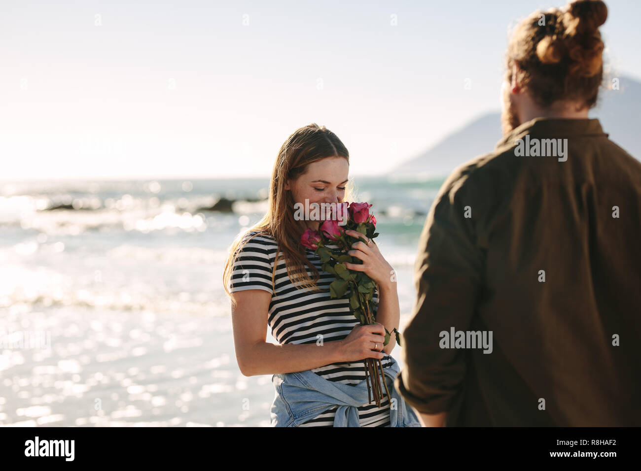 Attractive Woman holding Flowers donnée par son petit ami avec mer en arrière-plan. Friends sur date romantique sur la plage. Banque D'Images