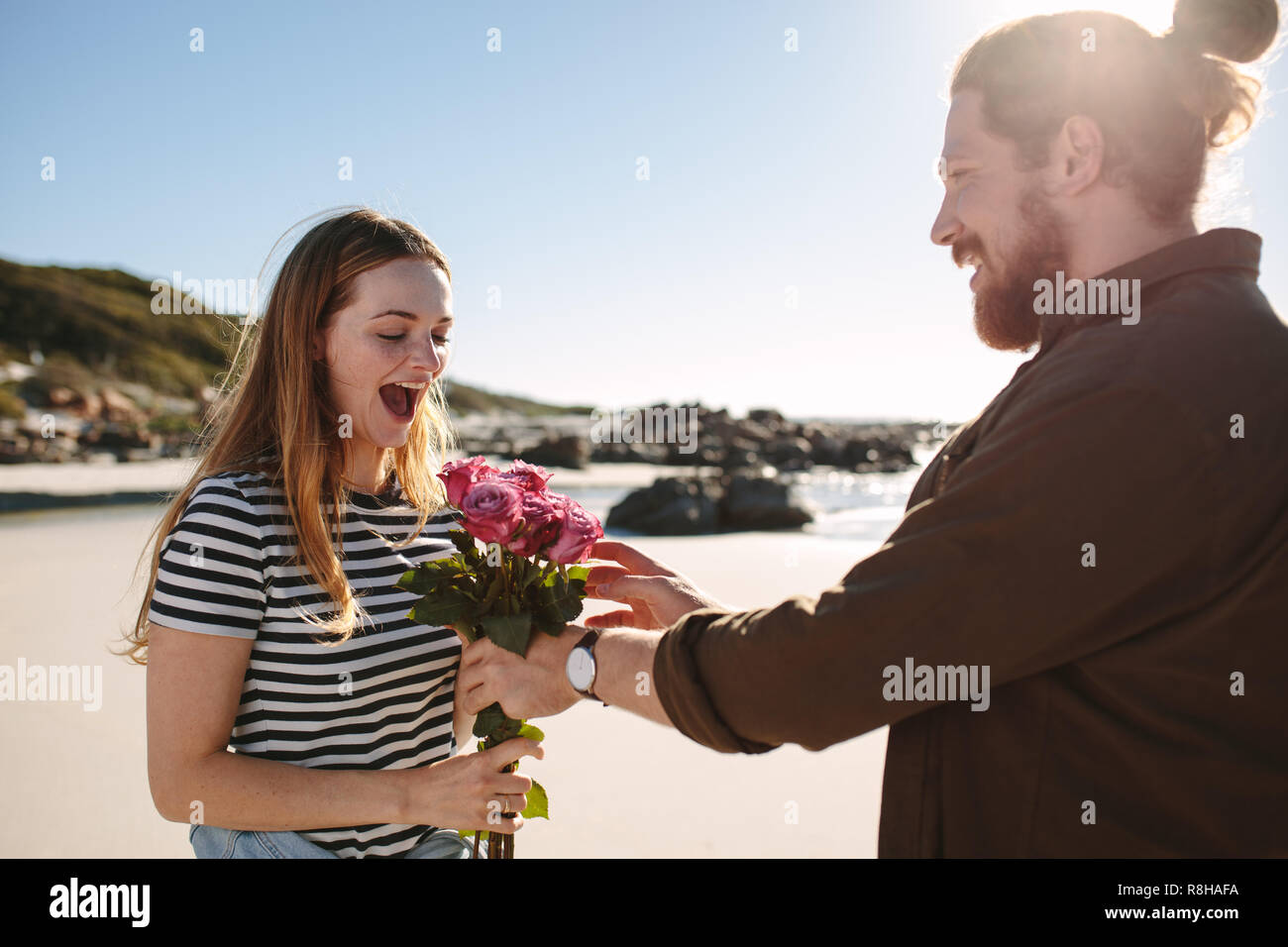 Surprenant petit ami petite amie avec des fleurs sur la plage. Surprenant l'homme femme avec bouquet de roses sur une date romantique. Banque D'Images