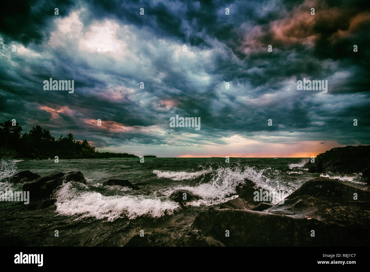 Ciel menaçant au-dessus du lac Supérieur dans la Péninsule Supérieure du Michigan. Moody colorés comme le coucher du soleil les vagues déferlent sur une plage de rochers. Seascape sombre arrière-plan. Banque D'Images