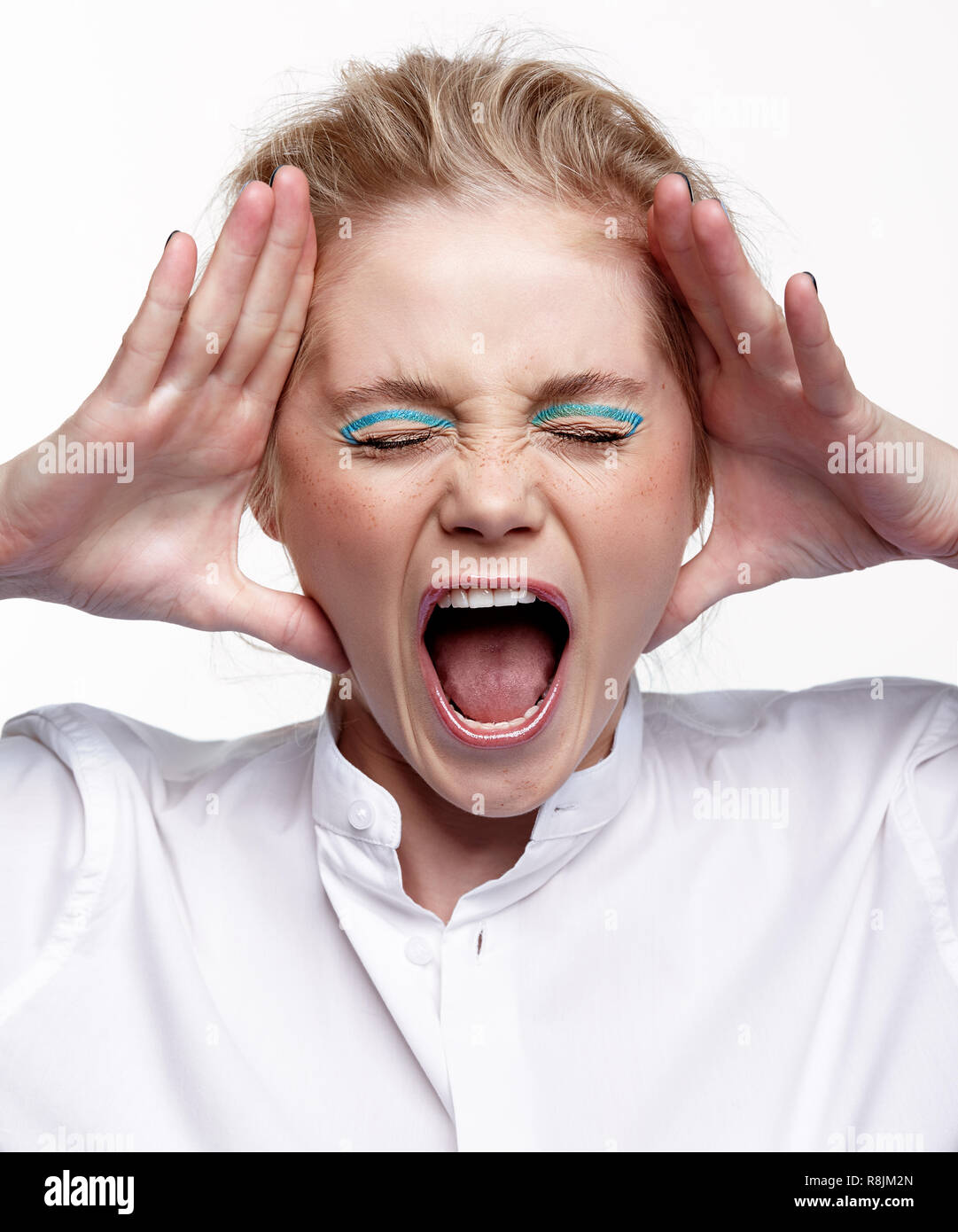 Portrait psychologique d'une jeune femme blonde sur fond gris. Les paumes à mettre visage et crier haut et fort Banque D'Images