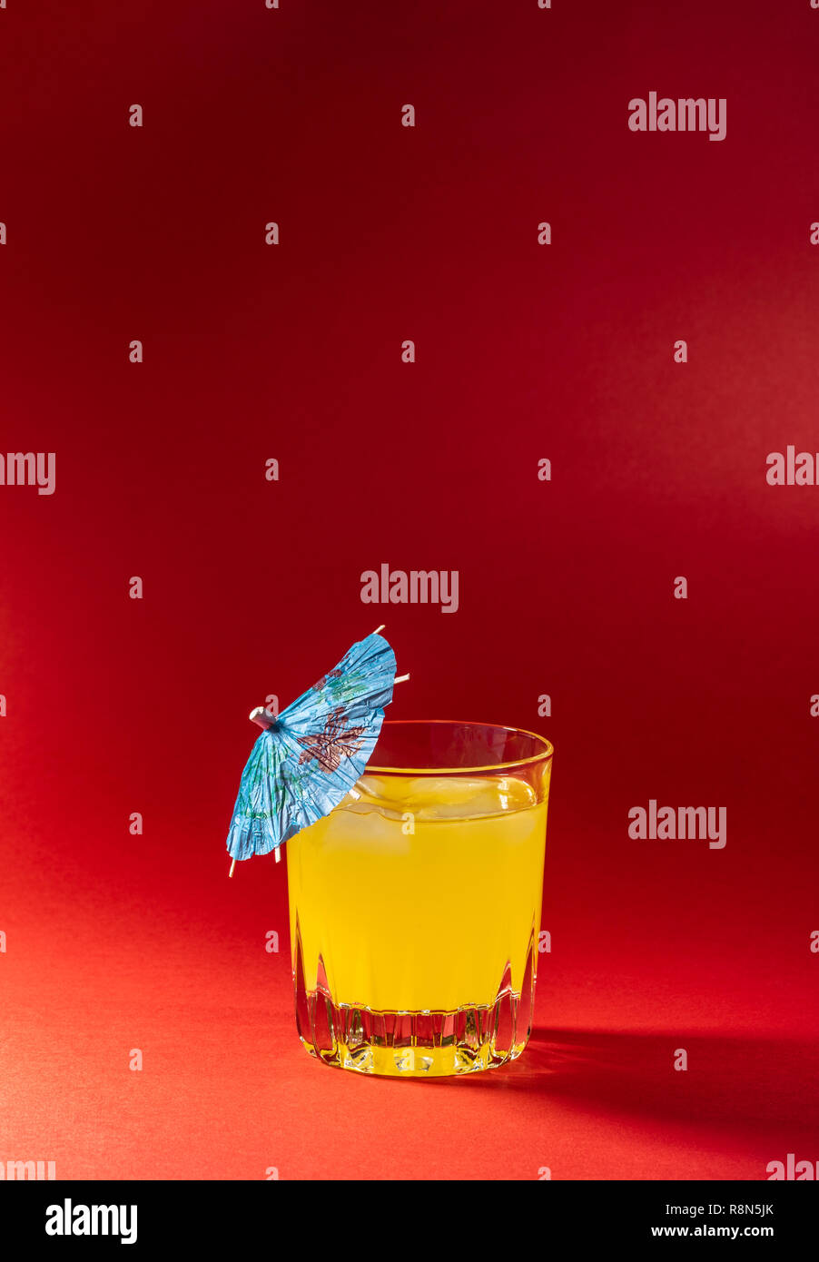 Boisson à l'orange sur fond rouge avec parapluie. Fruits à boire avec un cocktail d'un parapluie. Banque D'Images