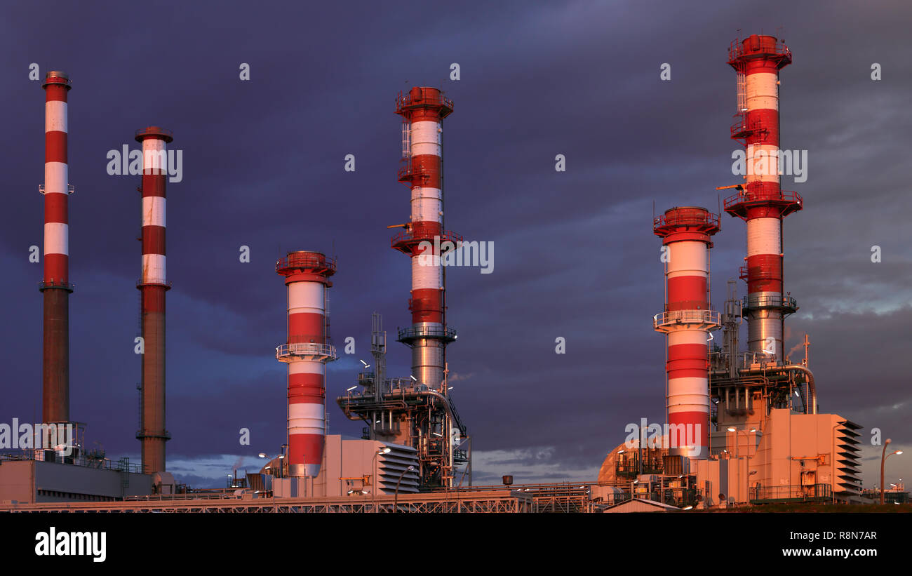 Une partie des nombreuses cheminées d'une grande raffinerie de pétrole dans un ciel couvert nuit Banque D'Images