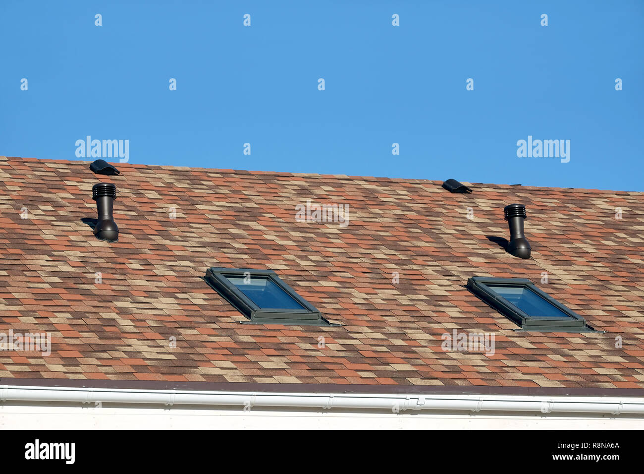 Fenêtres de toit et les tuyaux de ventilation résidentielle sur maison couverte de bardeaux motley soft close up view Banque D'Images