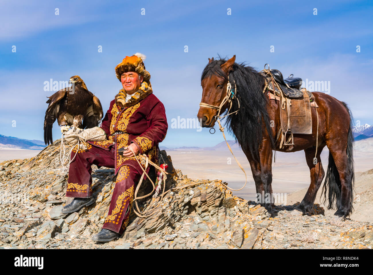 ULGII, LA MONGOLIE - le 9 octobre 2018 : Mongolian Golden Eagle Hunter avec son cheval et bien formé d'un aigle doré assis sur le sommet de la montagne prêt Banque D'Images