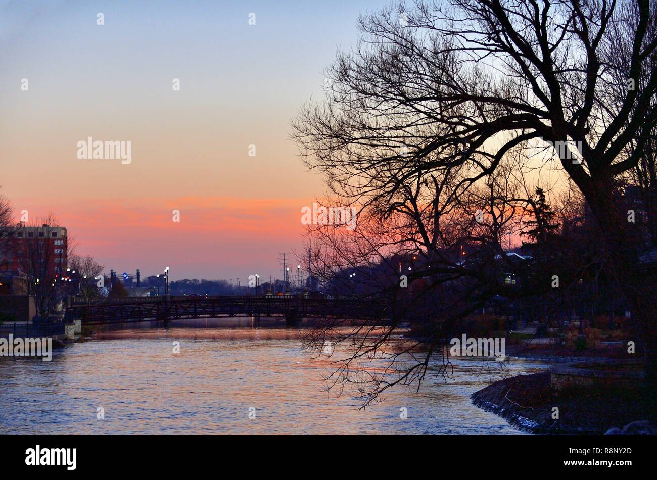 Elgin, Illinis, USA. Allume le long des rues et des ponts enjambant la rivière Fox comme crépuscule : coucher de soleil dans la ville de la rivière. Banque D'Images