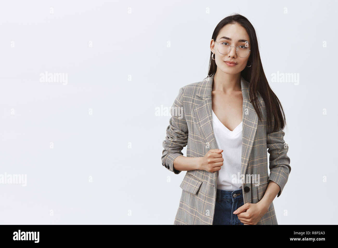 Confiant et réussie avocate prête à résoudre tout problème. Portrait de femme à la mode féminine élégante en manteau et lunettes, souriant poliment à l'appareil photo et l'article sur fond gris Banque D'Images
