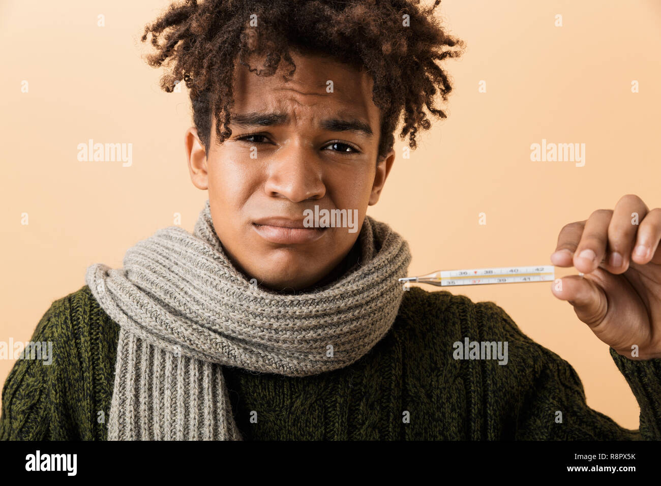 Portrait d'un jeune homme habillé en Afrique de l'automne vêtements isolated over beige background, thermomètre holding Banque D'Images