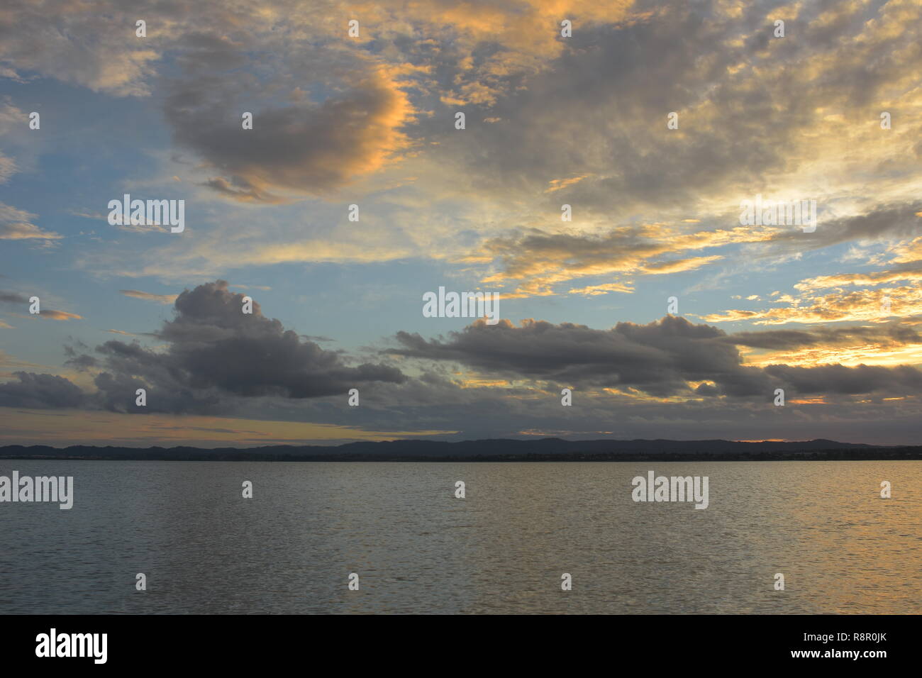 La surface calme de port de Waitemata reflétant la lumière du soleil avec terre lointaine en arrière-plan par temps nuageux en soirée. Banque D'Images