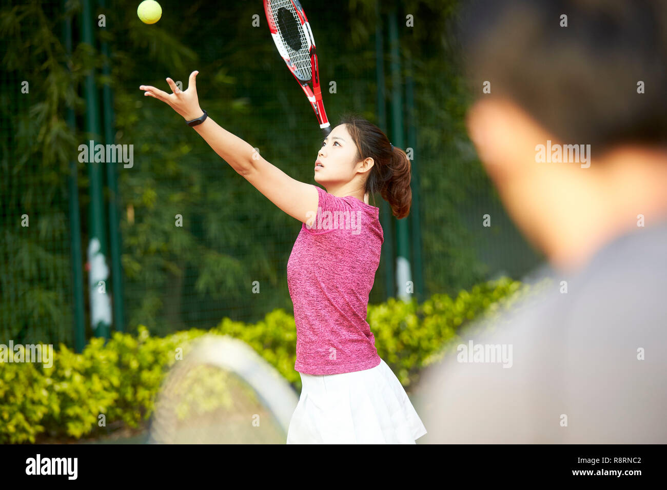 Jeune joueur de tennis asiatique de sexe féminin travaillant avec l'entraîneur sur le service Banque D'Images