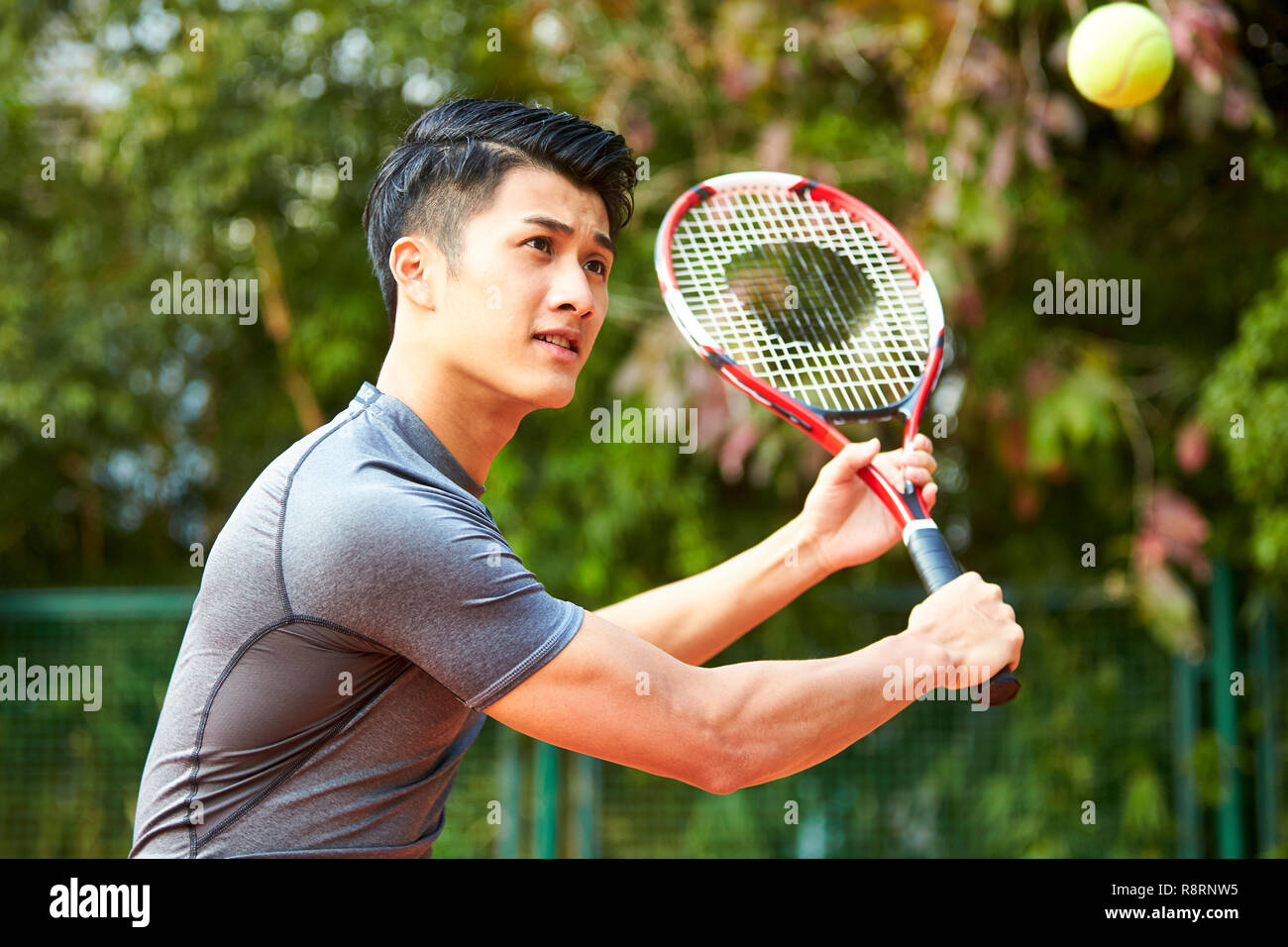 Young Asian male tennis player hitting ball avec un revers Banque D'Images