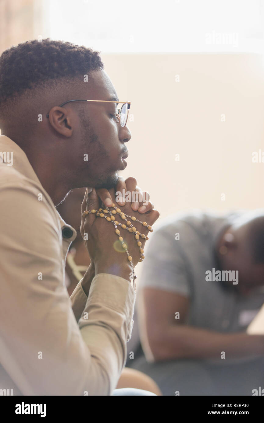 Jeune homme serein en prière avec le chapelet en groupe de prière Banque D'Images