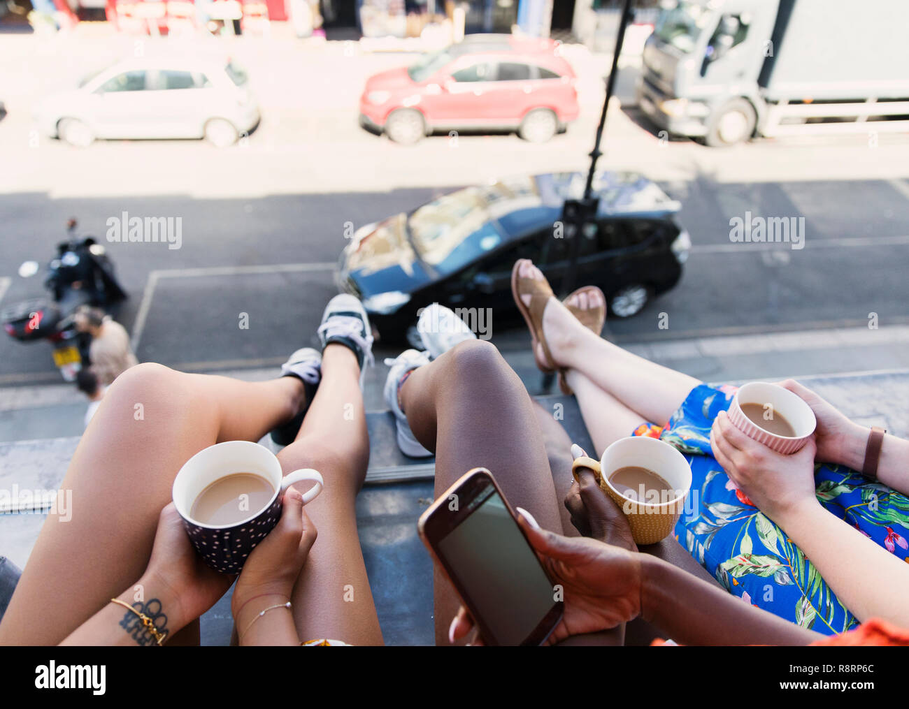 Les femmes les amis de boire du café, les jambes pendantes hors fenêtre appartement urbain Banque D'Images