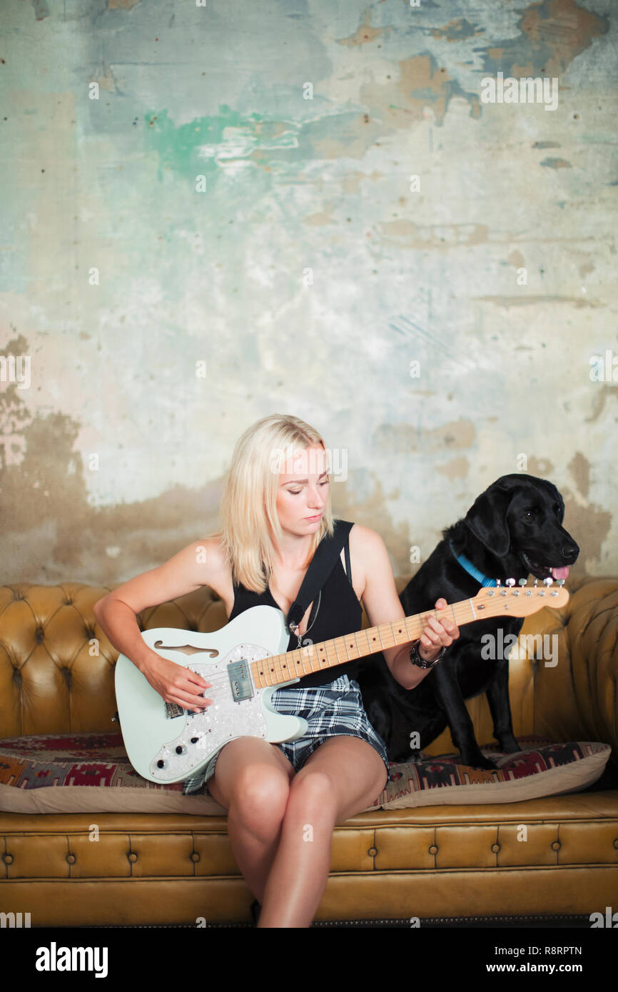 Jeune femme avec chien playing electric guitar on sofa Banque D'Images