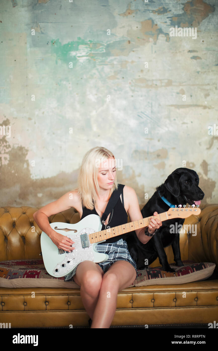 Jeune femme avec chien playing electric guitar on sofa Banque D'Images Jeune femme avec chien playing electric guitar on sofa Banque D'Images