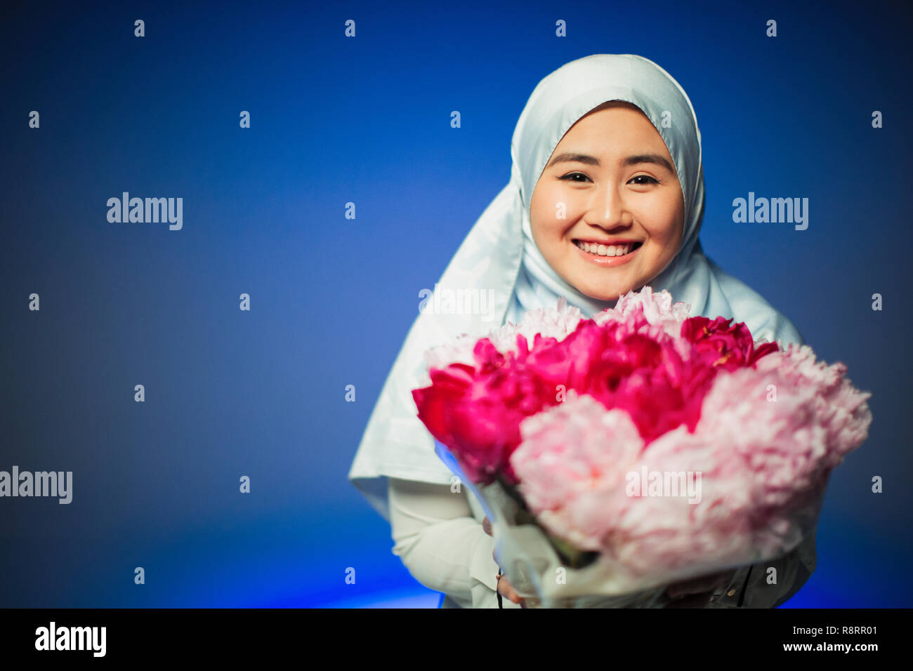 Portrait souriant, confiant jeune femme en hijab holding pivoines rose Banque D'Images