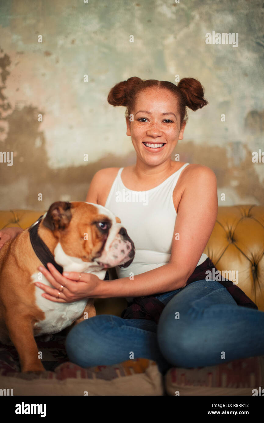 Portrait of smiling young woman petting dog on sofa Banque D'Images