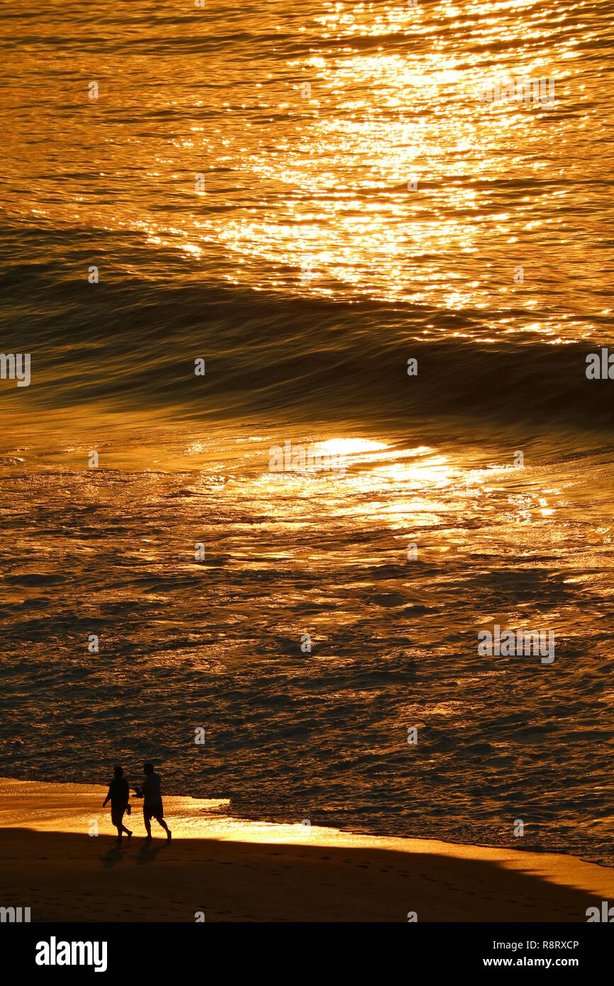 Océan Atlantique dans la lumière du soleil du matin d'or réflexions avec silhouette de deux personnes marchant sur la plage de Copacabana, Rio de Janeiro, Brésil Banque D'Images