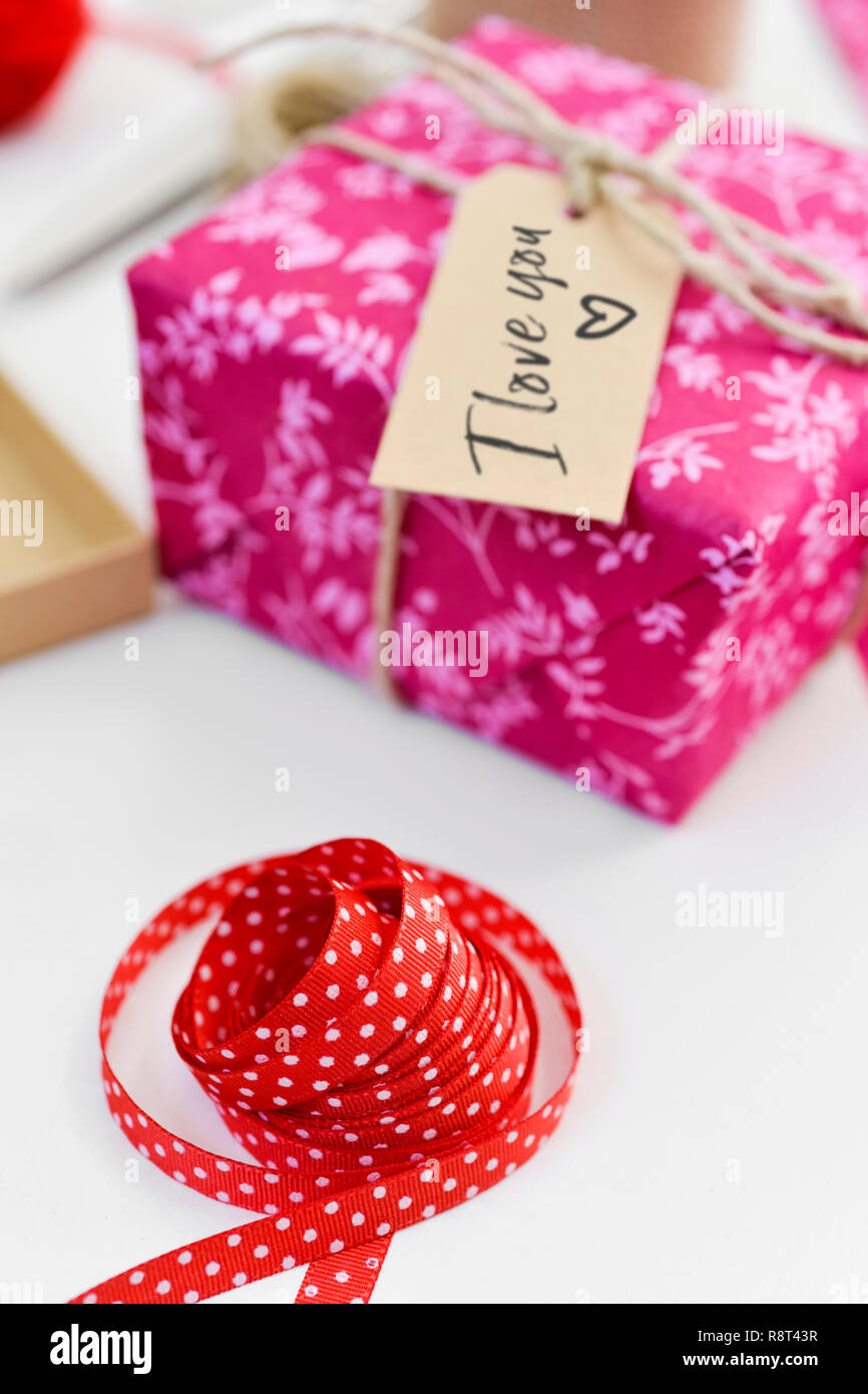 Un joli cadeau, emballé dans un papier rose et attachées avec une chaîne et  un brown étiquette liée à celui-ci avec le texte je t'aime écrit en C, sur  un tableau blanc