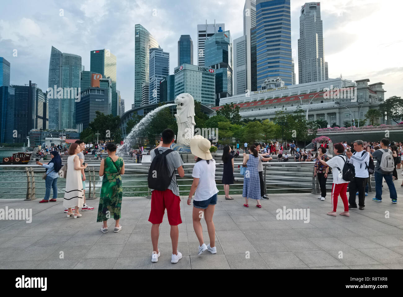 Les touristes asiatiques s'assemblant autour du Merlion, la moitié-moitié de poisson-lion statue, au Parc Merlion, Singapour ; zone. : le quartier des banques & Fullerton Hotel Banque D'Images
