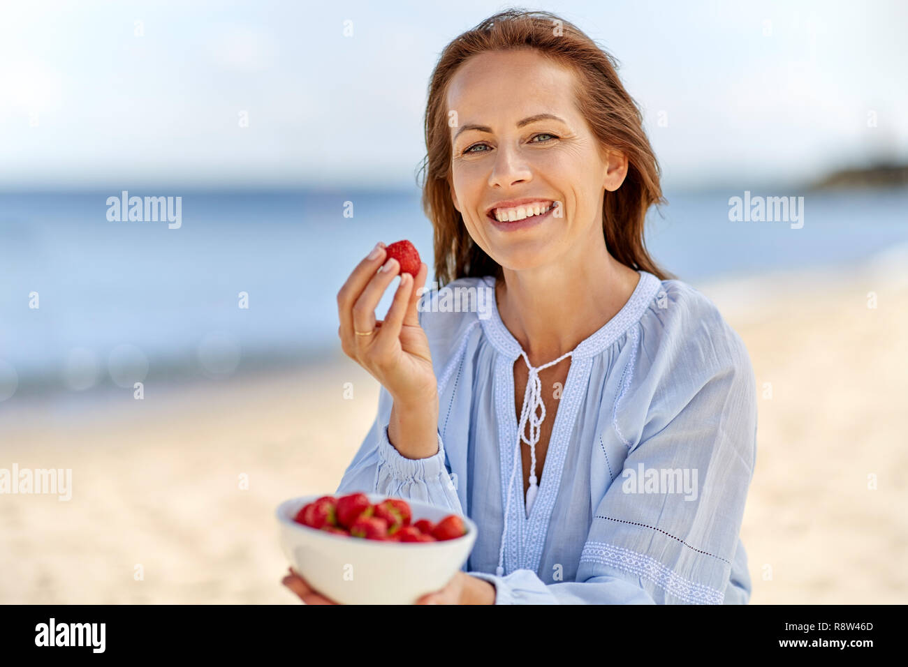 Happy woman eating strawberries on été plage Banque D'Images